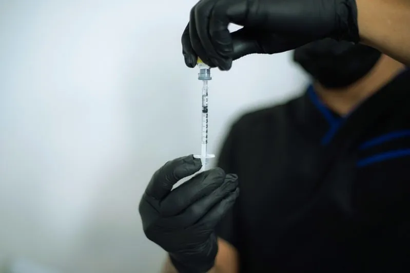 A gloved provider preparing a syringe in a clinical setting